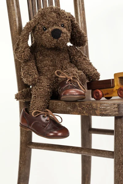 Милый мягкий игрушечный щенок, сидящий на стуле в старой кожаной обуви — стоковое фото